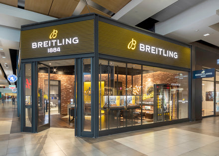 Breitling watch store with glass walls, yellow signage, and brick interior in a shopping mall.
