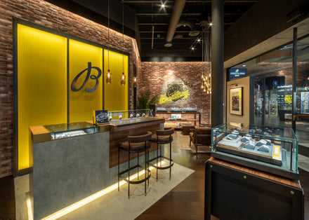 Luxury watch store interior with display cases, seating area, and exposed brick walls, warmly lit.