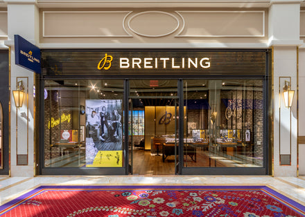 Storefront of Breitling with glass doors, illuminated sign, and displays of luxury watches inside.