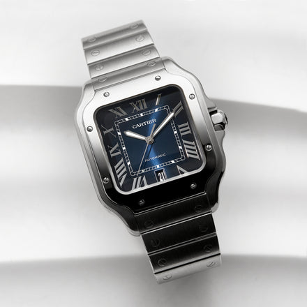 A Cartier Santos watch with a blue dial and Roman numerals on a stainless steel bracelet.