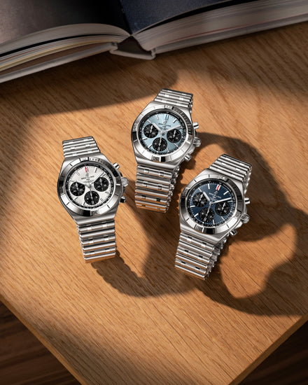 Three silver watches on a wooden surface with an open book in the background