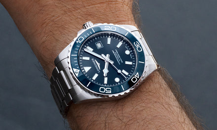 Wrist wearing a silver watch with a blue face on a dark background