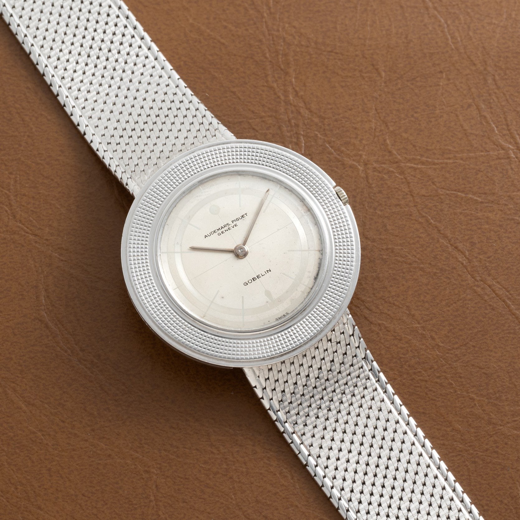 Audemars Piguet Signed Disco Volante Dress Watch Gübelin with a silver mesh bracelet and white dial displayed on a brown leather surface.
