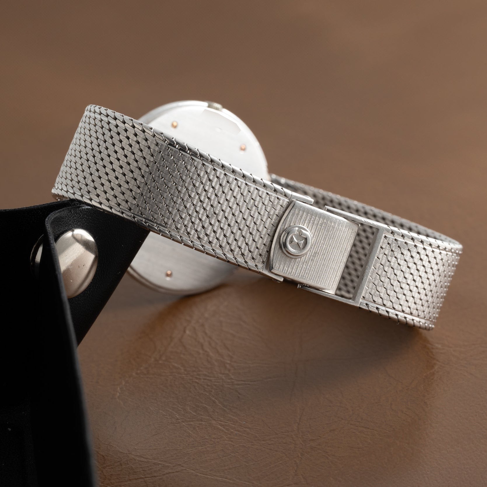 A close-up of the Audemars Piguet Signed Disco Volante Dress Watch Gübelin, featuring a silver mesh band with clasp, resting on a brown leather surface.
