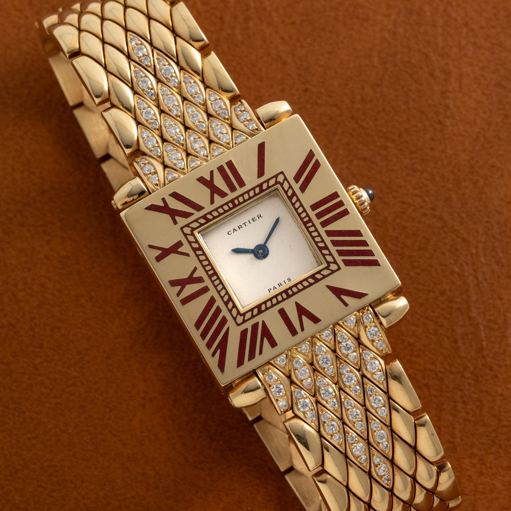 Gold-tone Cartier Obus watch with square cream dial, burgundy Roman numerals, diamond-set quilted bracelet, and blue hands.