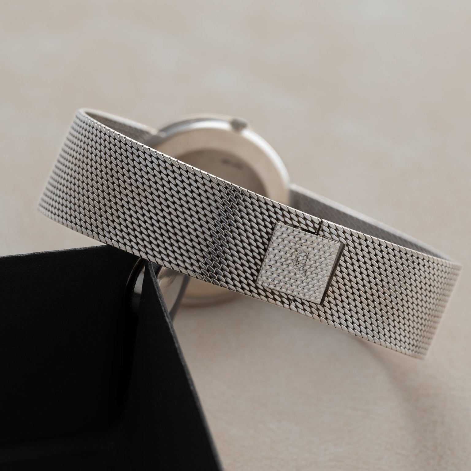Piaget’s Lapis Lazuli Dress Watch with a silver mesh band and square clasp rests on a light surface beside its black box.