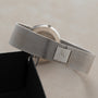 Piaget’s Lapis Lazuli Dress Watch with a silver mesh band and square clasp rests on a light surface beside its black box.