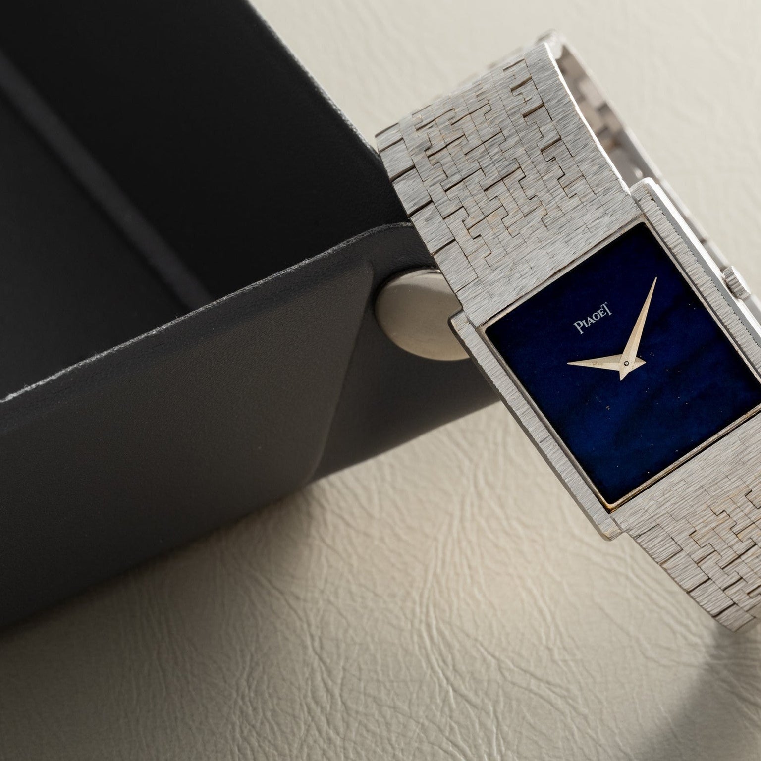 A white gold Piaget Lapis Lazuli dress watch with a blue rectangular face rests on the edge of a black tray.
