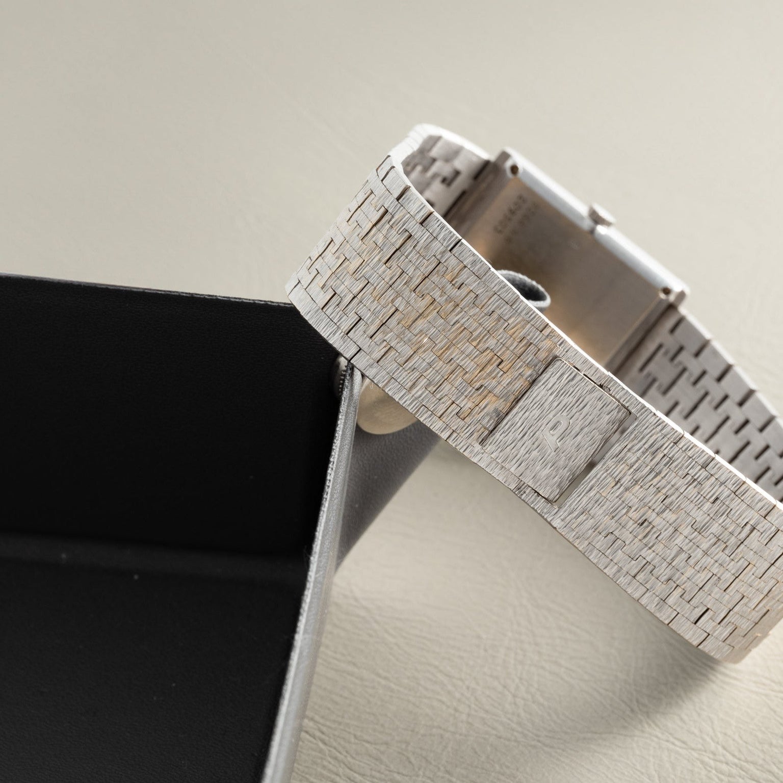 The Piaget White Gold Lapis Lazuli Dress Watch with a textured metal band rests on a black box, displayed on a light surface.