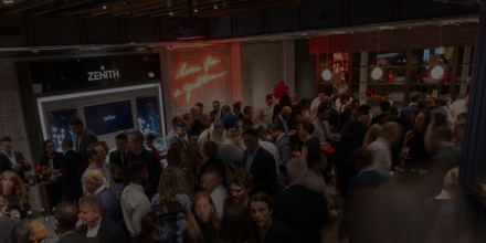 A crowded indoor event with people socializing near a Zenith store display and neon wall sign.