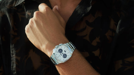 Close-up of a person wearing a silver wristwatch and a black patterned shirt, hand near collar.