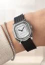 Luxury watch with black strap and diamond accents on a wrist, against a neutral background