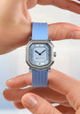 Luxury watch with blue strap held by a hand against a light background