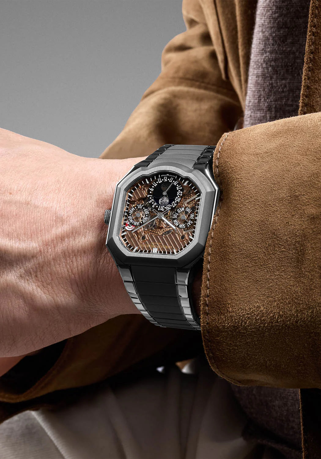 Luxury watch on a person's wrist with a brown jacket