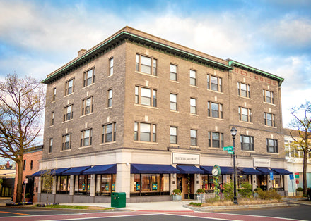 Four-story brick building with blue awnings and shops at street level on a sunny day.