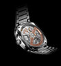 Silver-toned watch with exposed tourbillon mechanism, rose-gold accents, and metal link bracelet on black background.