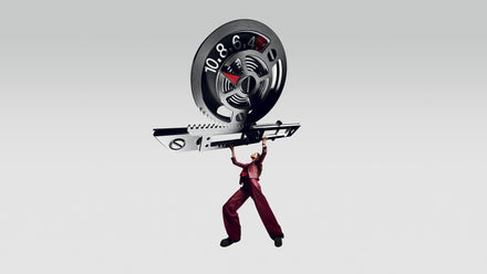 A person in red hangs from a giant film reel against a plain, light gray background.
