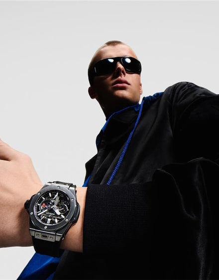 A person in sunglasses and a black jacket shows off a large, modern wristwatch.
