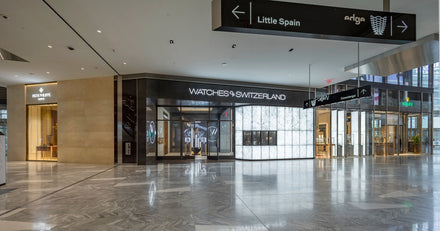 Interior of a modern mall with Watches of Switzerland and Rolex stores, and wayfinding signs above.