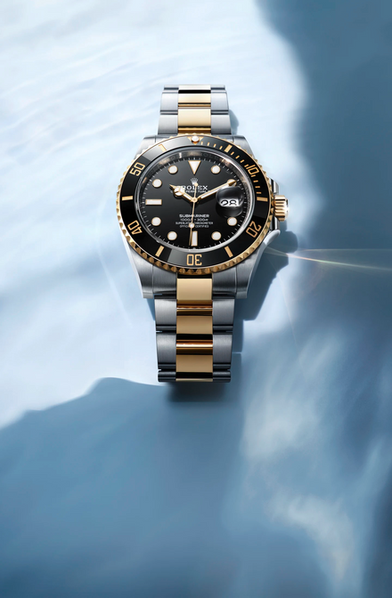 Black, silver, and gold Rolex Submariner on a blue background