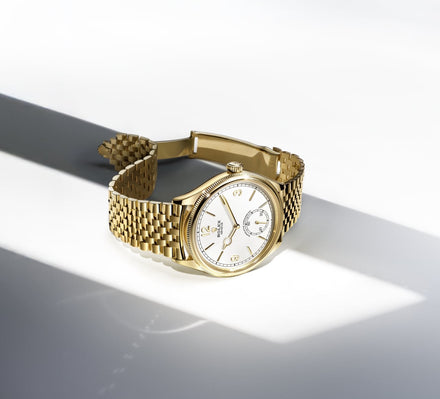 Gold Rolex 1908 watch on a grey and white geometric background