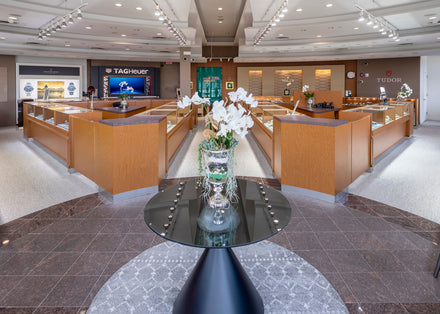 A modern jewelry store interior with wooden display cases and a glass table with white flowers in the center.