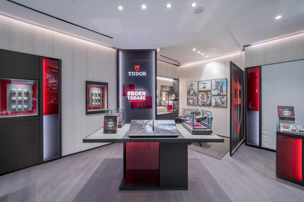 Modern Tudor watch boutique interior with display cases, red and black accents, and a #BORN TO DARE sign.