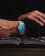 Person wearing a silver watch with a blue face on an open book