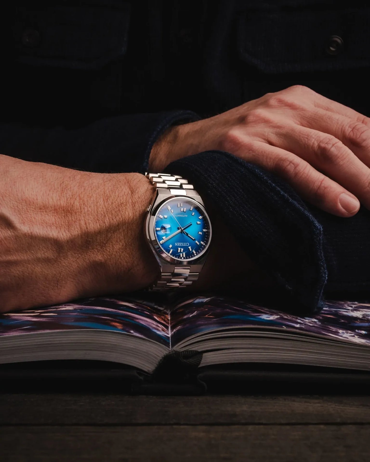 Person wearing a silver watch with a blue face on an open book