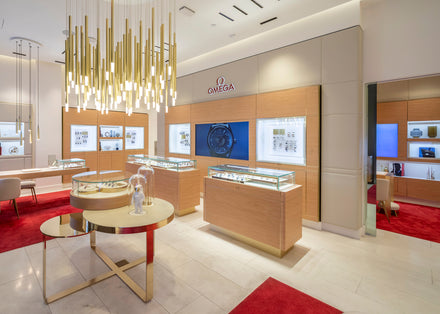 A modern Omega watch store interior with display cases, gold lighting, and red carpet accents.