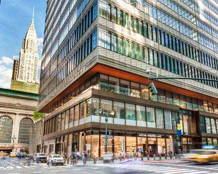 Busy city street with modern glass building, Grand Central, and Chrysler Building in the background.