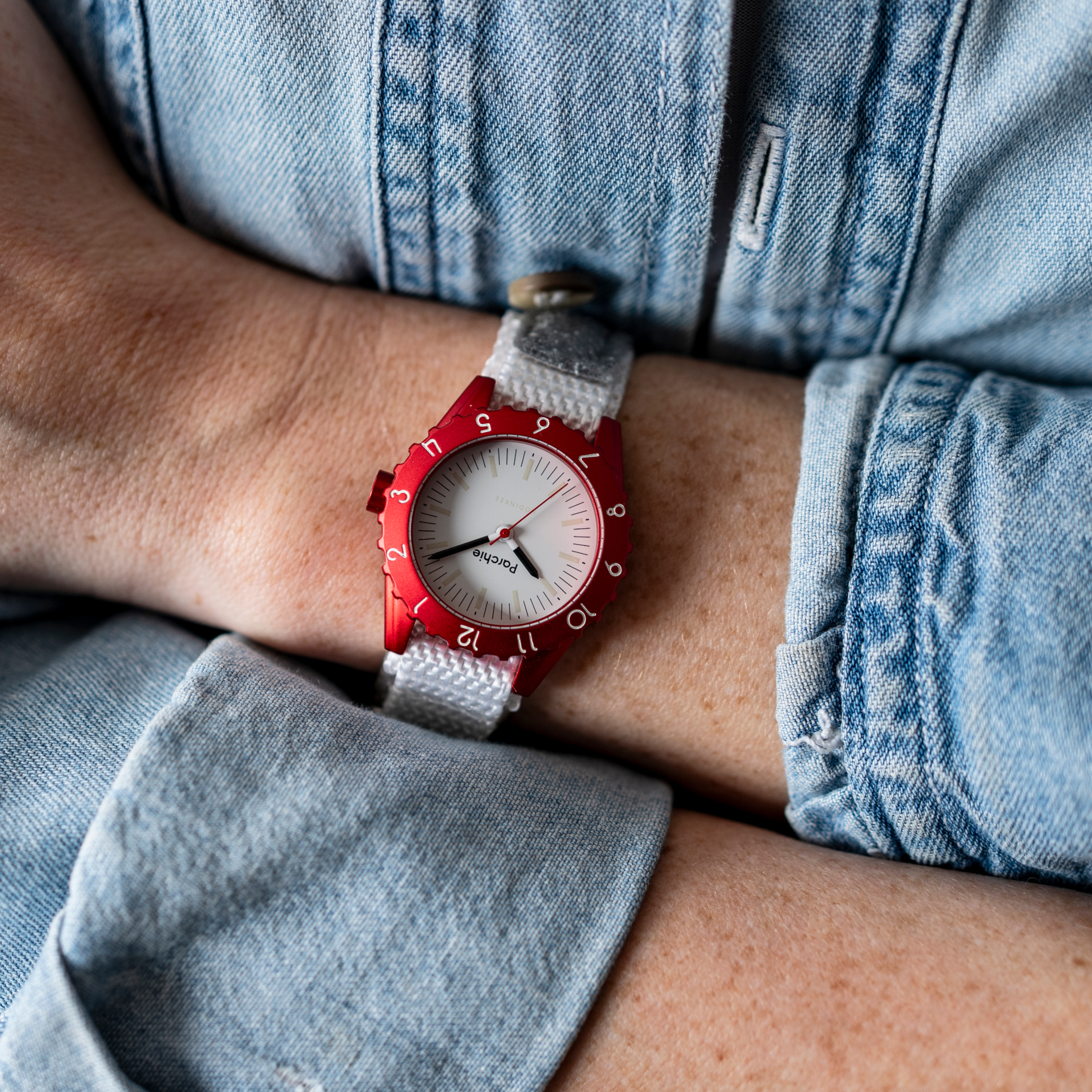 Close-up of a woman wearing the Parchie Lunar-Time Limited Editions for Hodinkee 32 wristwatch and a light blue denim shirt with folded arms.