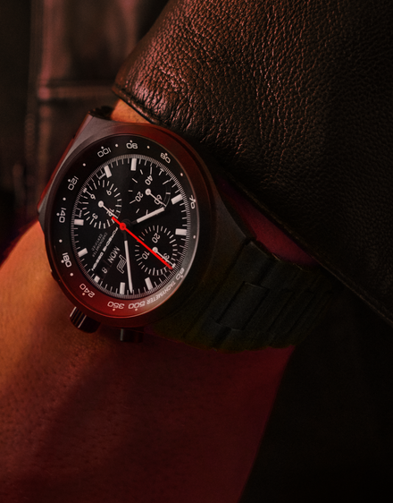 Close-up of a black chronograph watch with a red second hand on a wrist wearing a leather jacket.