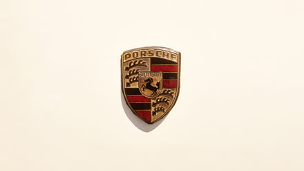 Porsche logo badge with a gold, black, and red shield design on a plain white background.