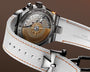 Stainless steel chronograph watch with bronze dial featuring ship's wheel design and white fabric strap with orange stitching