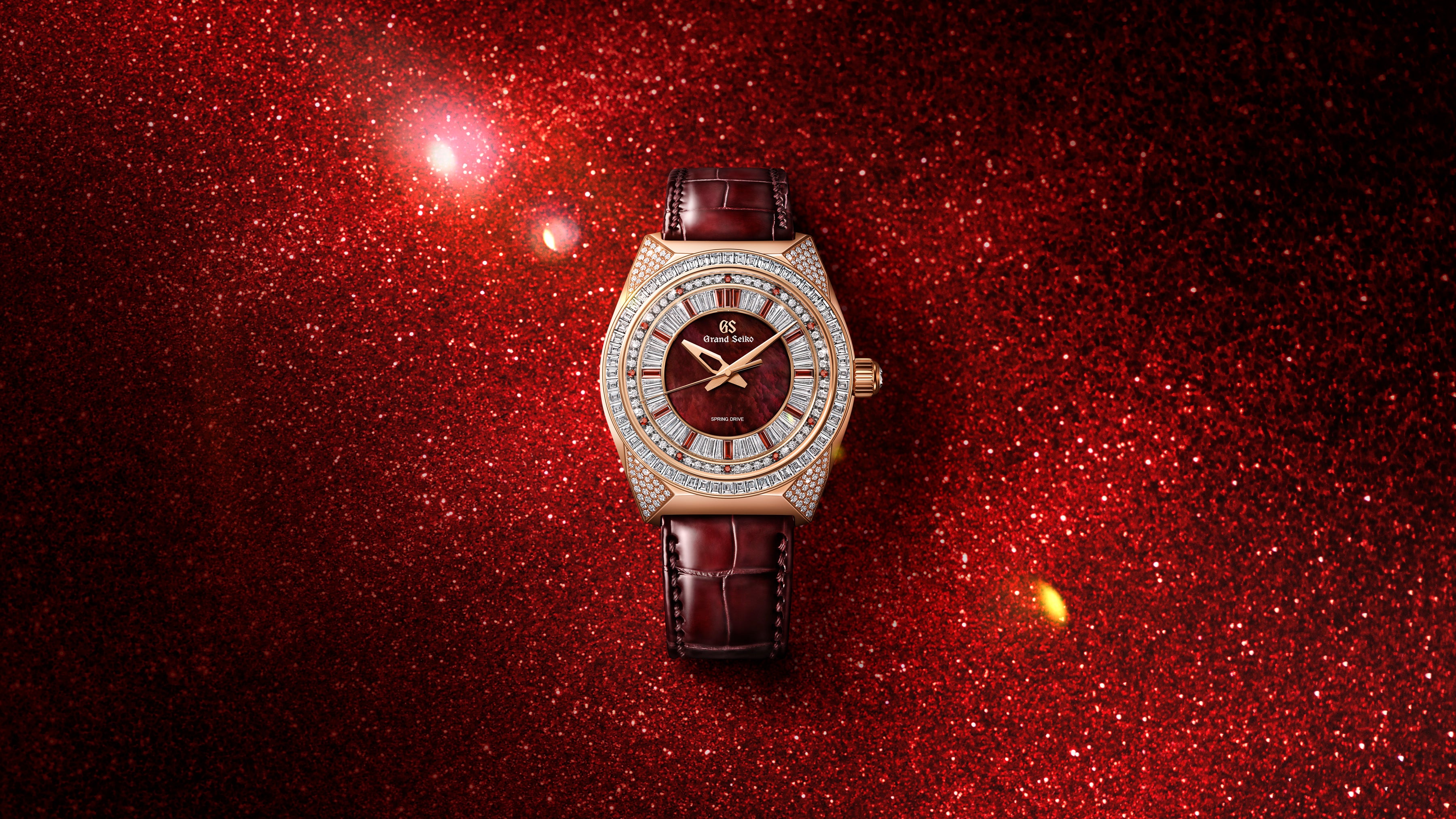 Luxury watch with burgundy dial, diamond-set bezel, gold-tone case, and burgundy leather strap on red glitter background.