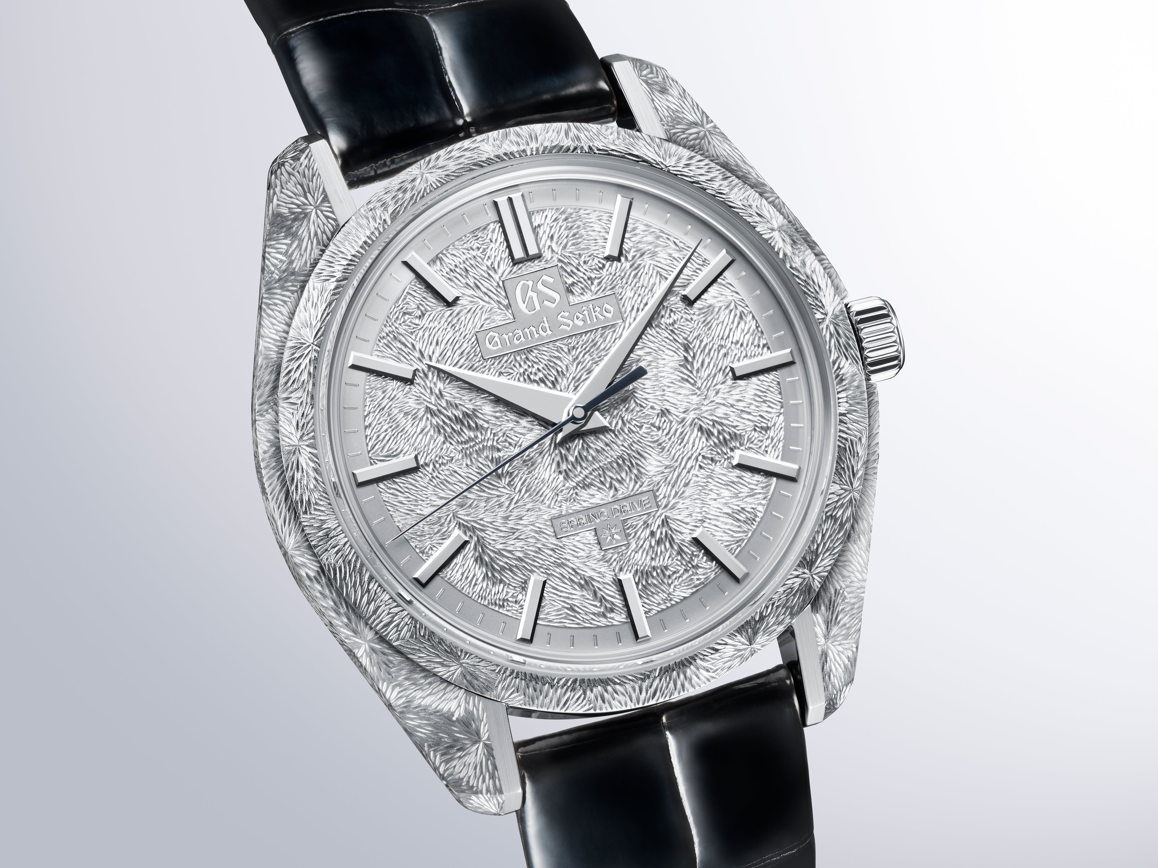 Silver-tone watch with textured case, patterned dial, applied hour markers, and black leather strap.