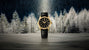 Gold-tone watch with black dial, black leather strap, and date window against a frost-covered forest backdrop.