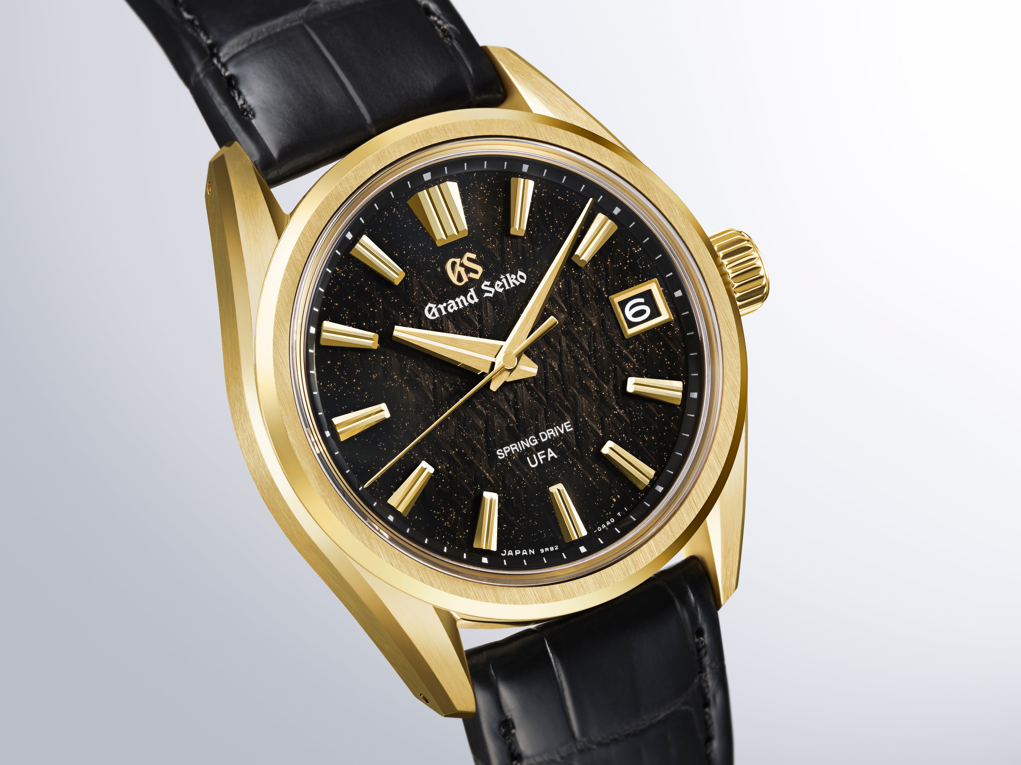 Gold-tone Grand Seiko watch with black dial, gold hour markers, date window, and black leather strap.