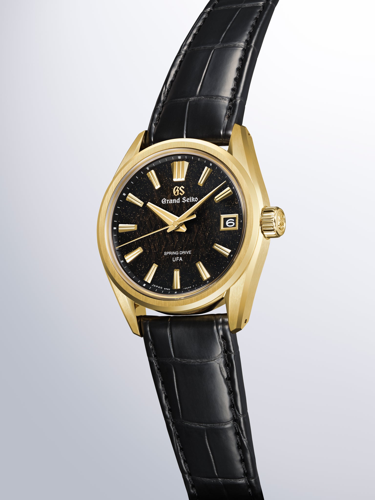 Gold-tone Grand Seiko watch with black dial, gold hour markers, date window, and black crocodile leather strap.