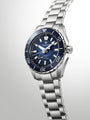 Silver and blue dive watch with dark blue dial, white hour markers, and matching blue rotating bezel on stainless steel brace