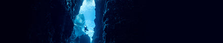 A diver swims between two dark underwater cliffs with sunlight filtering through blue water above.