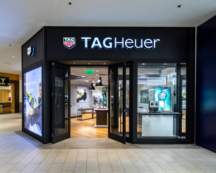 TAG Heuer store with glass doors, illuminated signage, and watch displays inside a shopping mall.