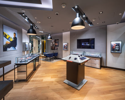 Modern watch boutique with glass display cases, wooden floor, wall art, and ambient lighting.