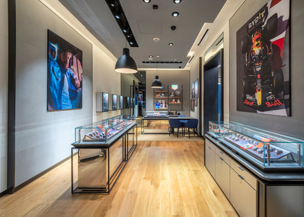Modern watch store interior with glass display cases, wood floors, and racing-themed wall art.