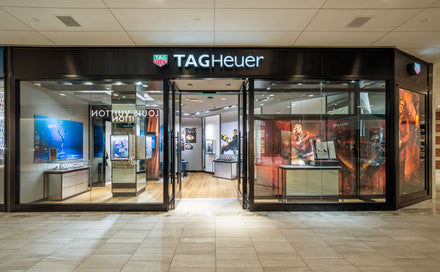 Tag Heuer store with glass front, watch displays, posters, and bright interior lighting.