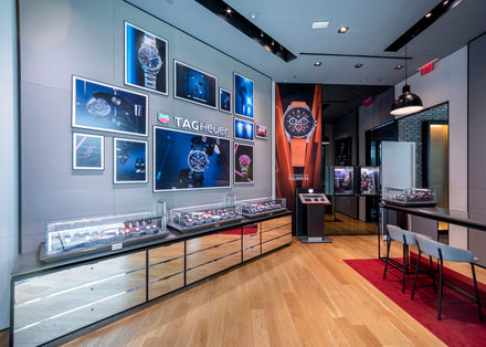 Modern TAG Heuer store interior with watch displays, branded wall art, and a seating area on a red rug.