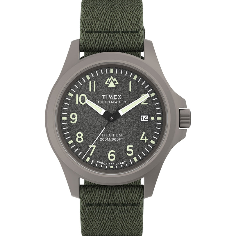 The Timex Expedition Titanium Automatic features a textured dark gray dial with white numerals and hands, date at 3 o’clock, titanium case (200M/660FT water-resistant, shock resistant), and a green fabric strap.