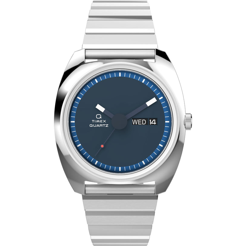 The Timex Q Timex 1975 Enigma Reissue is a silver quartz wristwatch with a blue dial, silver hour markers, day-date display (WED 14), stainless steel strap, and minimalist design.