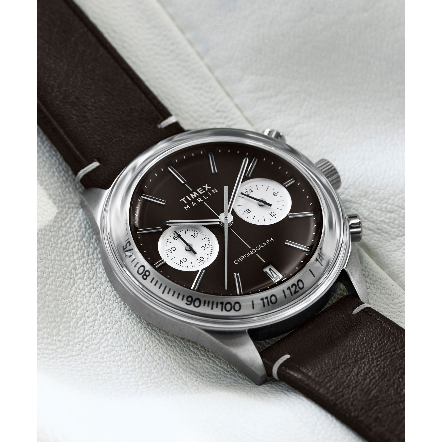 A close-up of the Timex G SS QZ SW JET 40 BROWN DL BWN STP 25 watch shows its dark brown dial, two white subdials, silver hands, and brown leather strap on a textured surface, channeling the retro-futuristic Marlin Jet Chronograph style.